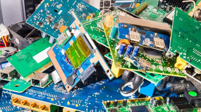 A pile of mixed electronic waste, including various circuit boards, USB ports, cables, and other electronic components, heaped together. The image shows different colors and configurations of electronic parts, suggesting the discard of numerous electronic devices.